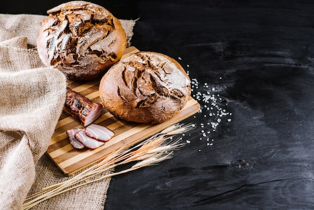 Sweet fresh bread and wheat on black wooden background