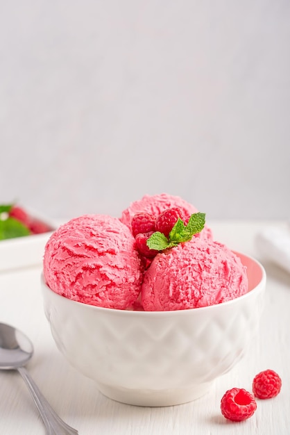 Sweet fresh frozen berry ice cream scoops in bowl with raspberries and mint leaf on white table