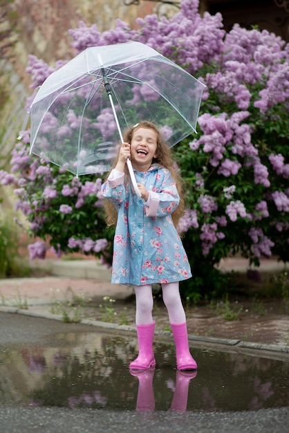 A sweet girl of five years with a transparent umbrella against the background of blooming lilacs