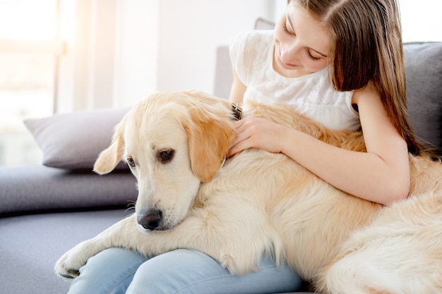 Sweet girl holding cute dog sitting on sofa indoors