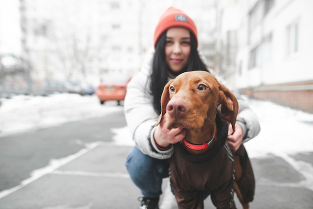 Sweet girl with a beautiful dog breed magyar vizsla sits on a winter street