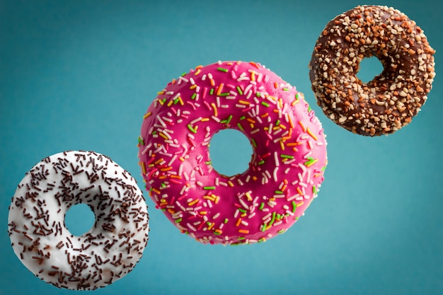 Sweet  glazed donuts flying over blue background, junk food concept