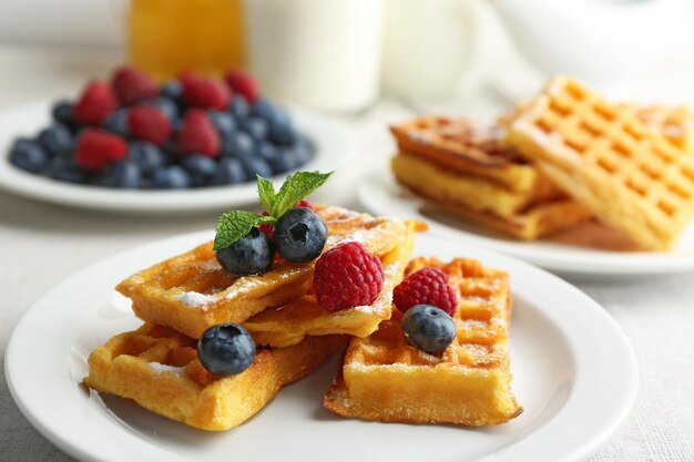 Sweet homemade waffles with forest berries and sauce on table background