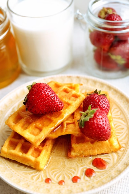 Sweet homemade waffles with fresh strawberries on plate on light background