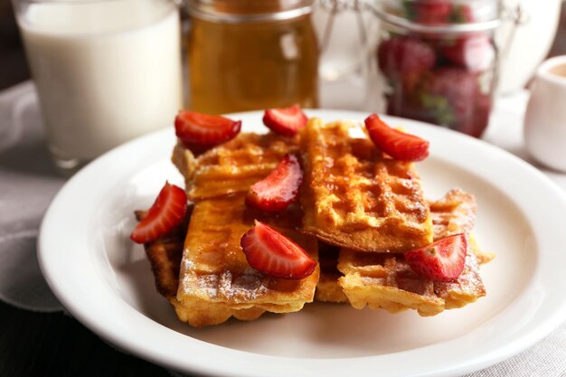 Sweet homemade waffles with strawberries on plate on table background