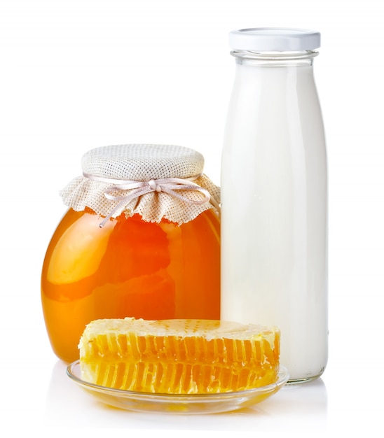 Sweet honey in glass jars with honeycombs and bottle of milk isolated