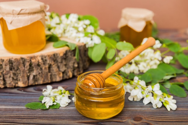 Sweet honey jar surrounded spring acacia blossoms Honey flows from a spoon in a jar jars of clear fresh acacia honey on wooden background