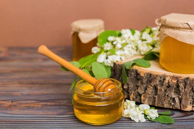 Sweet honey jar surrounded spring acacia blossoms Honey flows from a spoon in a jar jars of clear fresh acacia honey on wooden background