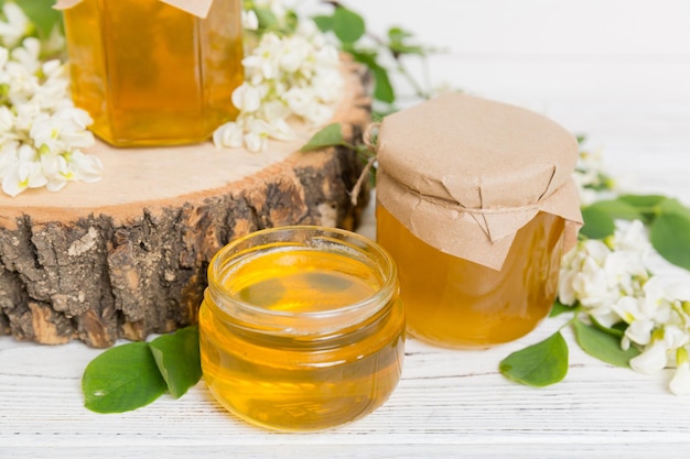 Sweet honey jar surrounded spring acacia blossoms Honey flows from a spoon in a jar jars of clear fresh acacia honey on wooden background