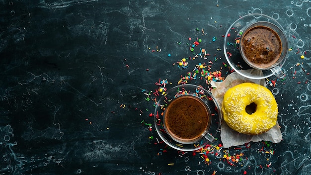 Sweet lemon yellow donut with a cup of coffee on a black stone table Top view