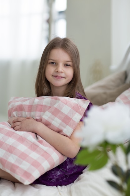 Sweet little dark hair girl with cushin sits on bed