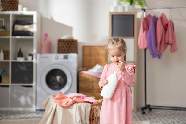 A sweet little girl plays in the laundry room bathroom next to the laundry basket with clothes