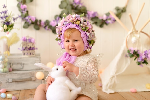 Sweet little girl with decoration on her head and colored Easter eggs on a white wooden background