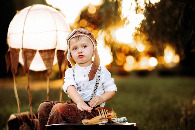 Sweet little pilot boy in vintage aviator hat sitting and playing with small wooden plane outdoor