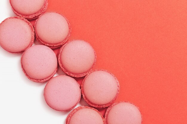 Sweet macaroons in row. Bright macaroon biscuits close up on paper background with copy space. Trend color "living coral". Top view.