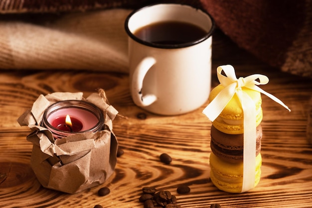 Sweet macaroons on wooden board with cup of coffee and a burning candle Atmospheric photo Content for social networks