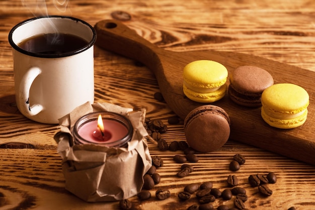 Sweet macaroons on wooden board with cup of coffee and a burning candle Atmospheric photo Content for social networks