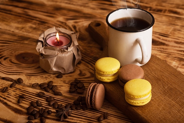 Sweet macaroons on wooden board with cup of coffee and a burning candle Atmospheric photo Content for social networks