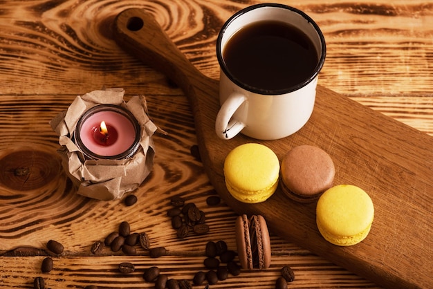 Sweet macaroons on wooden board with cup of coffee and a burning candle Atmospheric photo Content for social networks