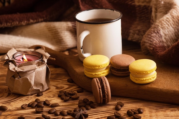 Sweet macaroons on wooden board with cup of coffee and a burning candle Atmospheric photo Content for social networks