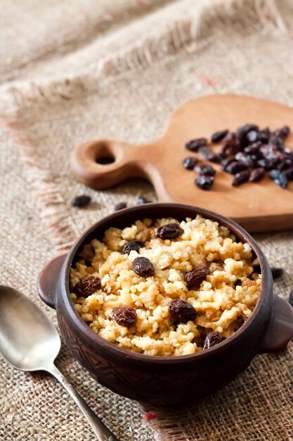 Sweet millet porridge with dark raisins in ceramic rustic bowl with walnuts on background. Copy space