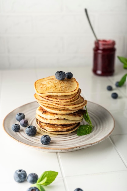 Sweet pancakes for breakfast in a stack on a ceramic plate with fresh blueberries and mint light key...