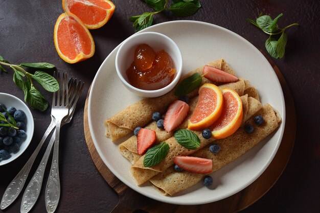 Sweet pancakes wrapped with fresh mint strawberries blueberries oranges and jam