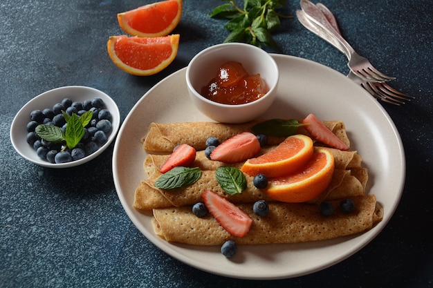 Sweet pancakes wrapped with fresh mint strawberries blueberries oranges and jam