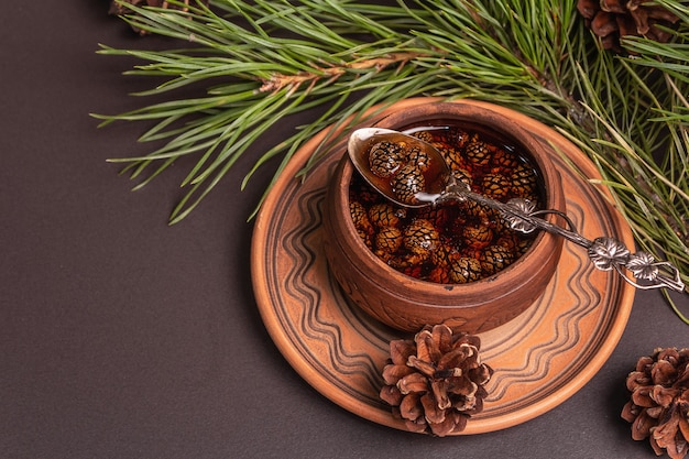 Sweet pine cone jam. Traditional Siberian dessert, fresh evergreen branches. Black stone concrete background, copy space