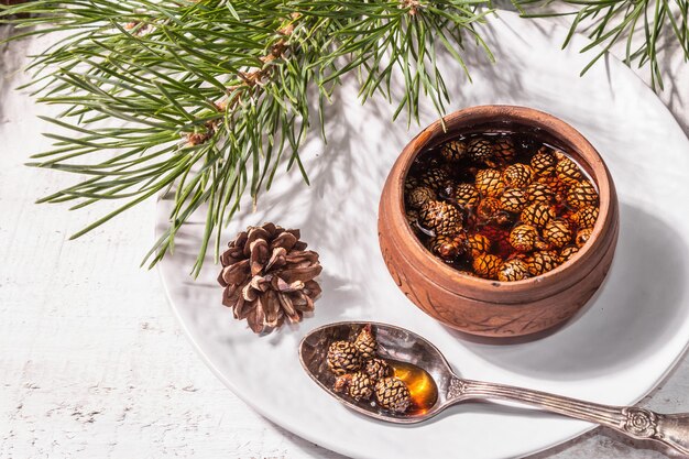 Sweet pine cone jam. Traditional Siberian dessert, fresh evergreen branches. Trendy hard light, dark shadow. White wooden background, copy space