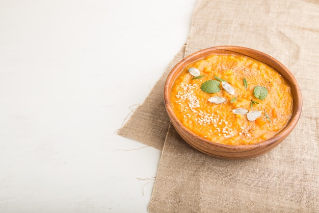 Sweet potato or batata cream soup with sesame seeds in a wooden bowl on a white wooden background. side view, copy space.