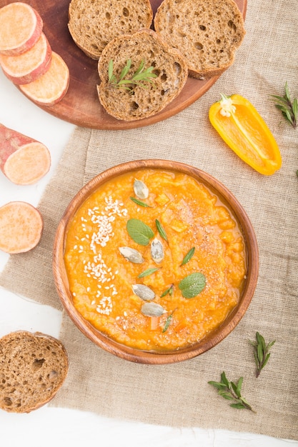 Sweet potato or batata cream soup with sesame seeds in a wooden bowl on a white wooden background. top view, close up.