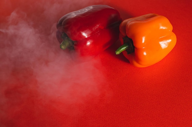 Photo sweet red and orange peppers on a red background with a light smoke