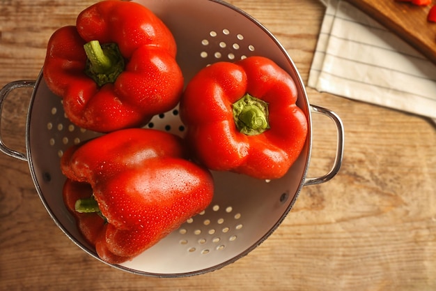 Sweet red peppers in colander on wooden background