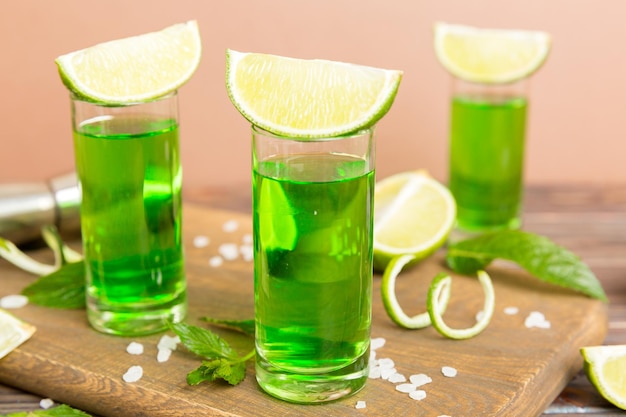 Sweet refreshing mint liqueur with ice and mint leaves on table background Shots with lime slice and mint flat lay