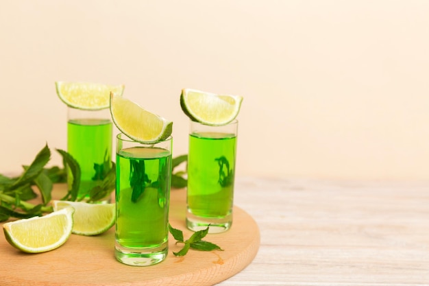 Sweet refreshing mint liqueur with ice and mint leaves on table background Shots with lime slice and mint flat lay