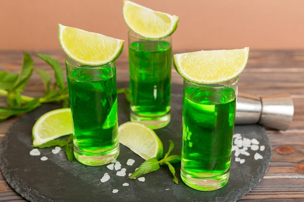 Sweet refreshing mint liqueur with ice and mint leaves on table background Shots with lime slice and mint flat lay