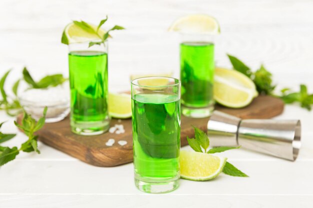 Sweet refreshing mint liqueur with ice and mint leaves on table background Shots with lime slice and mint flat lay