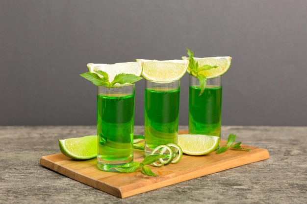 Sweet refreshing mint liqueur with ice and mint leaves on table background Shots with lime slice and mint flat lay