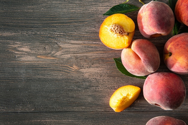 Sweet ripe juicy peaches with green leaves on a wooden background