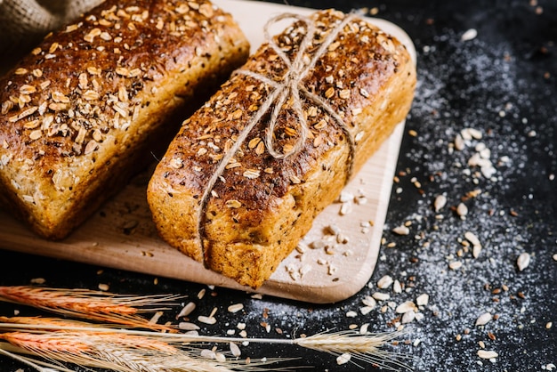 Sweet rye bread and wheat on black wooden background