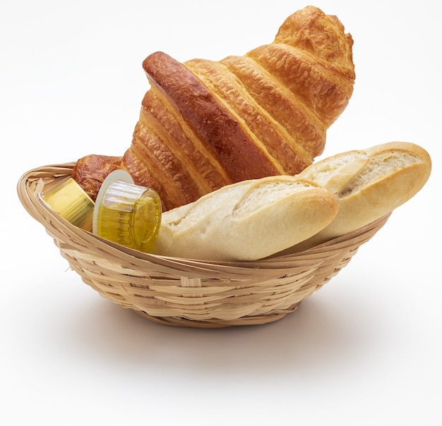 Sweet and salty breakfast. Wicker basket with Croissant, rolls, olive oil and jam. Isolated.