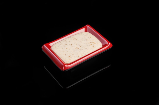 Sweet and sour spicy sauce for sushi rolls in a red bowl on a black background with reflection