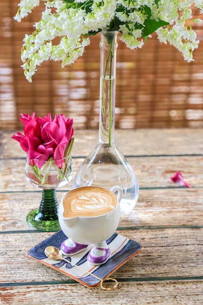 Sweet table setting with flowers and cup of hot latte on a wooden table