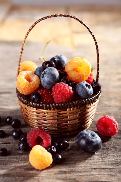 Sweet tasty berries in basket on wooden table close up