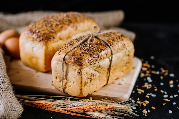 Sweet and tasty bread and wheat on black wooden background