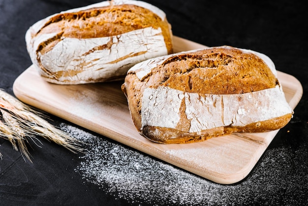 Sweet and tasty bread and wheat on black wooden background