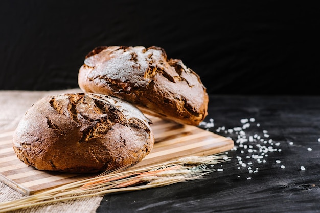 Sweet and tasty bread and wheat on black wooden background