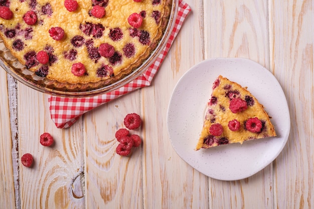 Sweet tasty pie with jellied and fresh raspberry fruits in baking dish and plate with red tablecloth towel