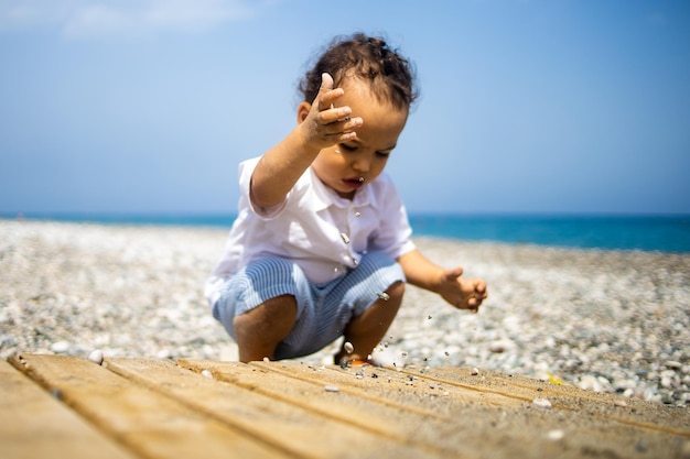 Sweet toddler boy playing with pebble on the beach near sea